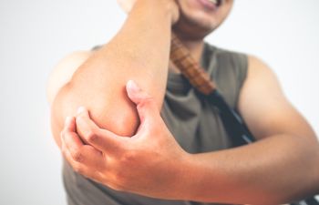 A man suffering form elbow pain holding a tennis racket under his arm.