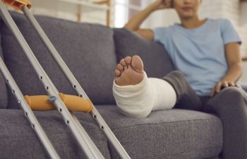 Crutches next to a person resting their broken leg on the sofa.