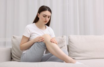 Young woman suffering from pain in knee on sofa at home. Space for text