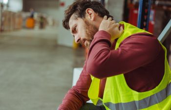 Tired, upset, sick bearded man, worker having neck and back pain, after work in warehouse, copy space. Concept of health care, treatment