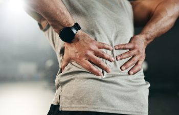Fitness, back pain and hands of man at gym for training with muscle, problem or arthritis. Sports, injury and guy athlete with joint massage for backache, fibromyalgia or osteoporosis accident.