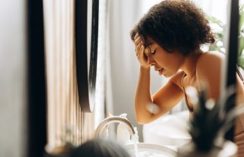 Young woman holding her head and leaning over the bathroom sink, suffering from a headache or migraine